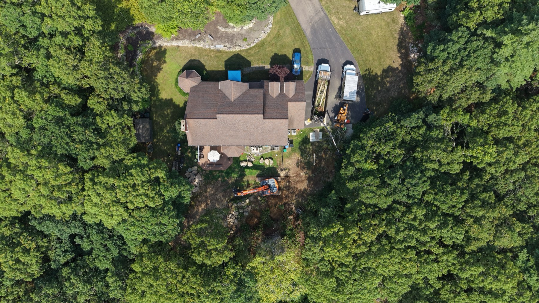 Overhead view of a home set in dense woodland, showing the full lot and driveway